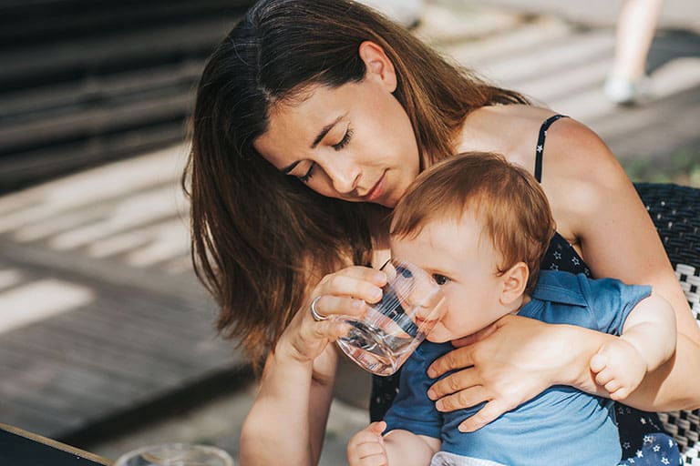 Madre y bebé en un café al aire libre, mamá dando agua al niño de un vaso