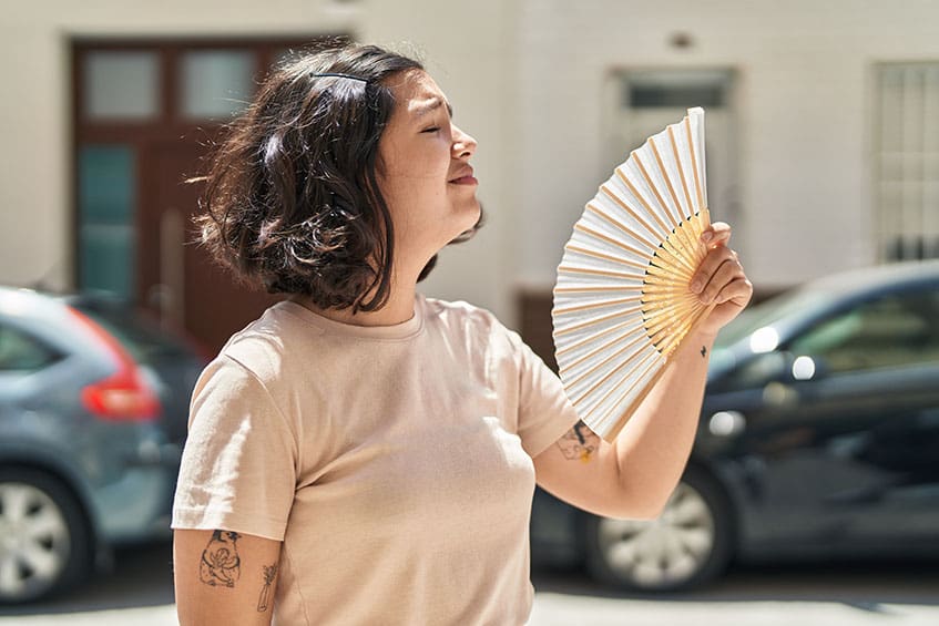 Молодая женщина использует ручной веер на улице